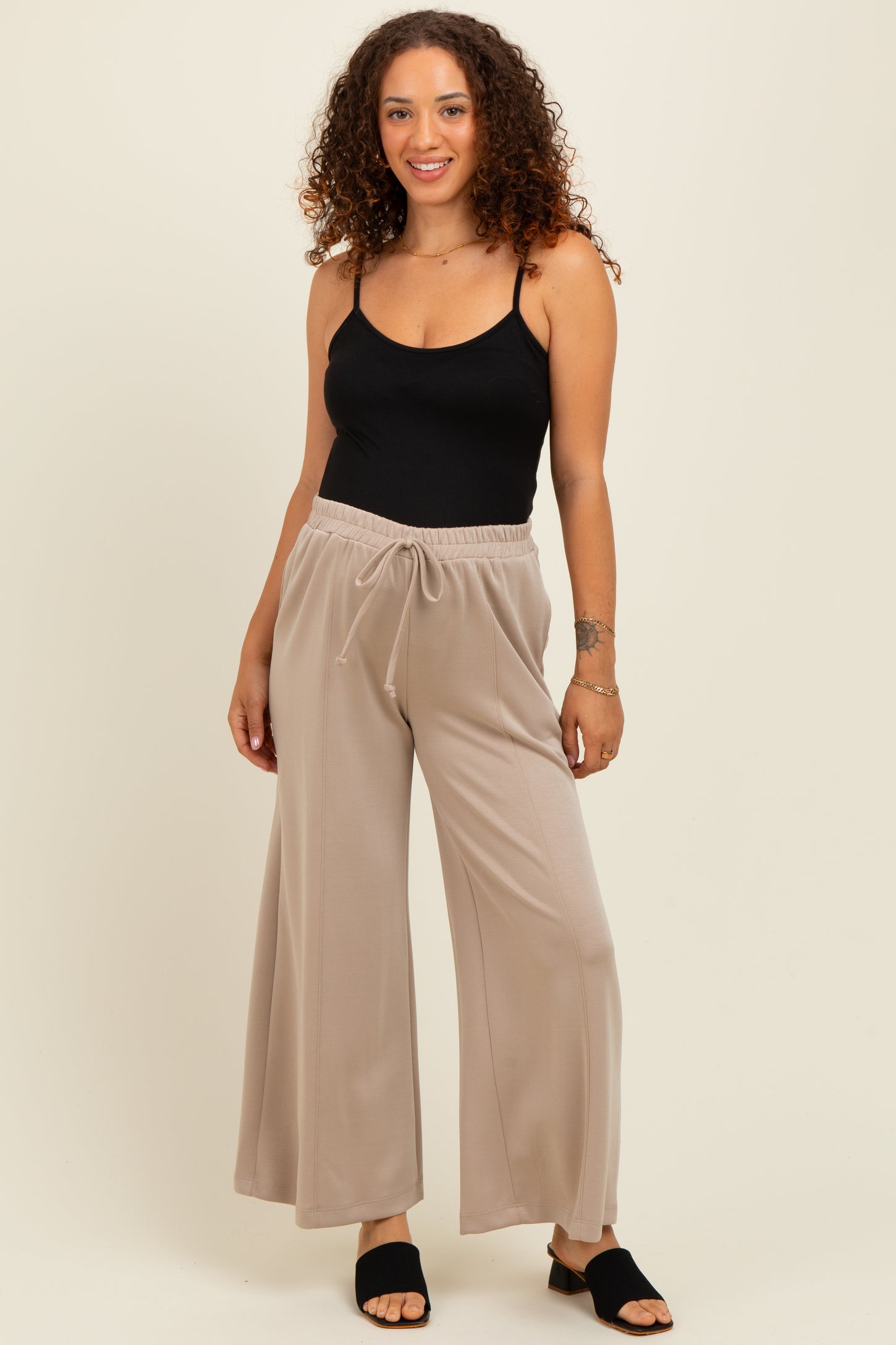woman wearing a black maternity tank top and beige wide-leg maternity pants with an elastic waistband