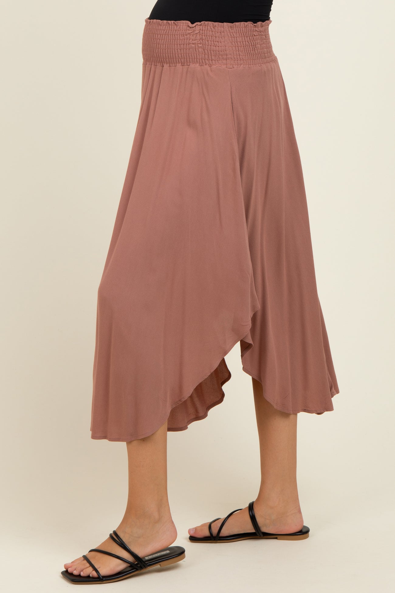 woman wearing a dusty rose maternity skirt with a smocked waistband and asymmetrical hemline, paired with flat black sandals