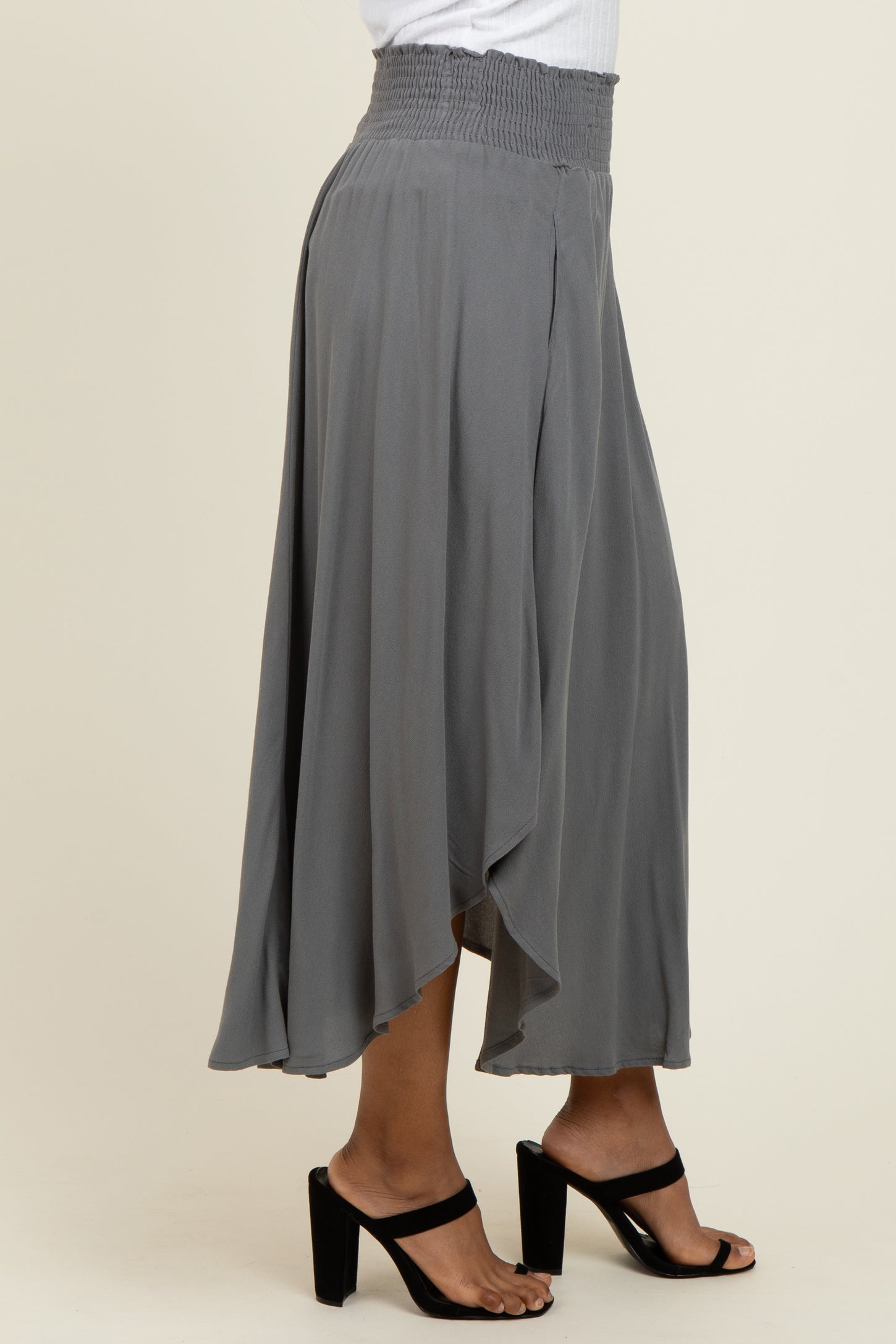 woman wearing a gray maxi skirt with a smocked waist and a flowy silhouette, styled with black block-heeled sandals
