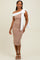 woman wearing a fitted beige midi dress with a white oversized bow on the shoulder and strappy heels