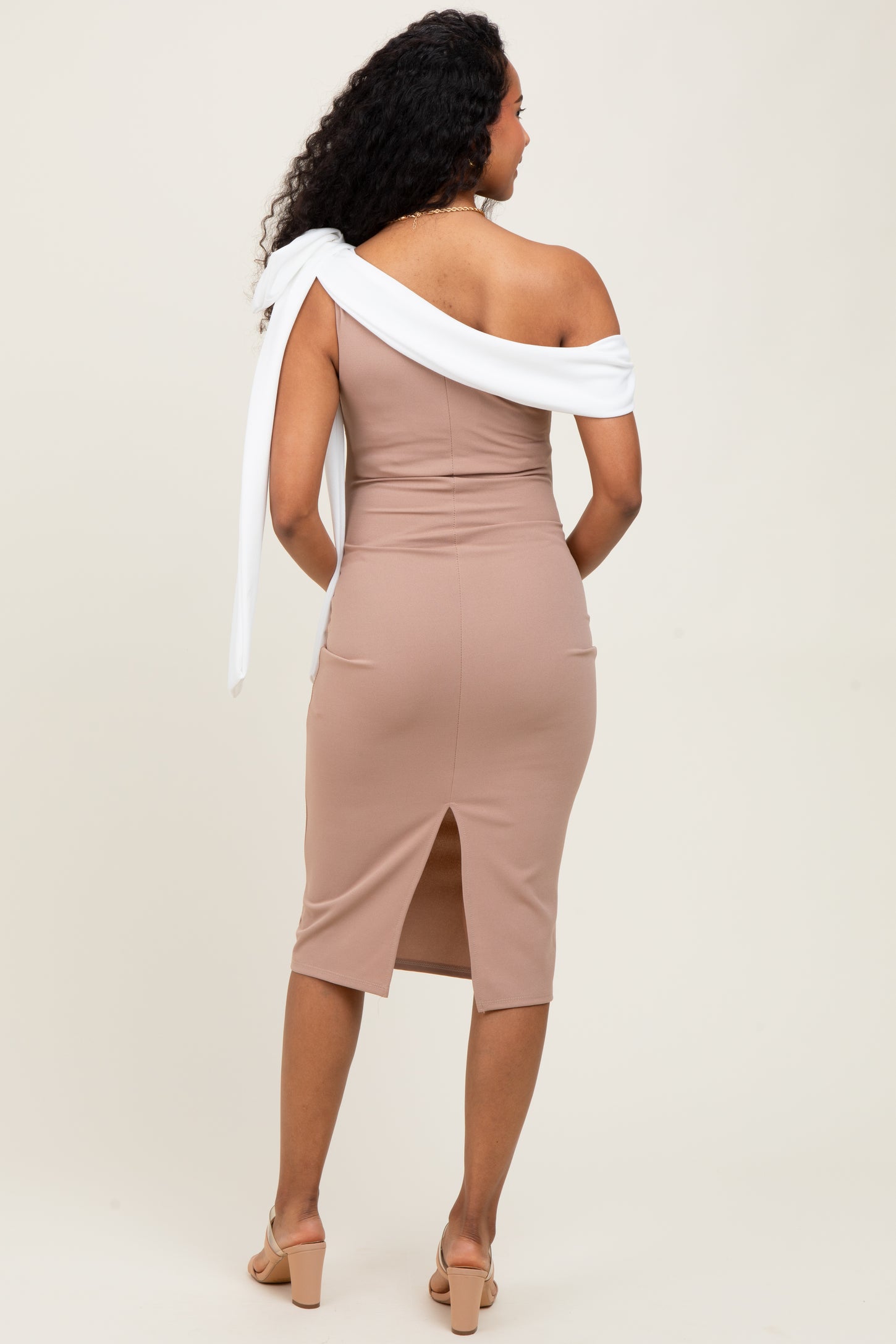 woman wearing a fitted beige maternity dress with an off-shoulder white tie detail and a back slit