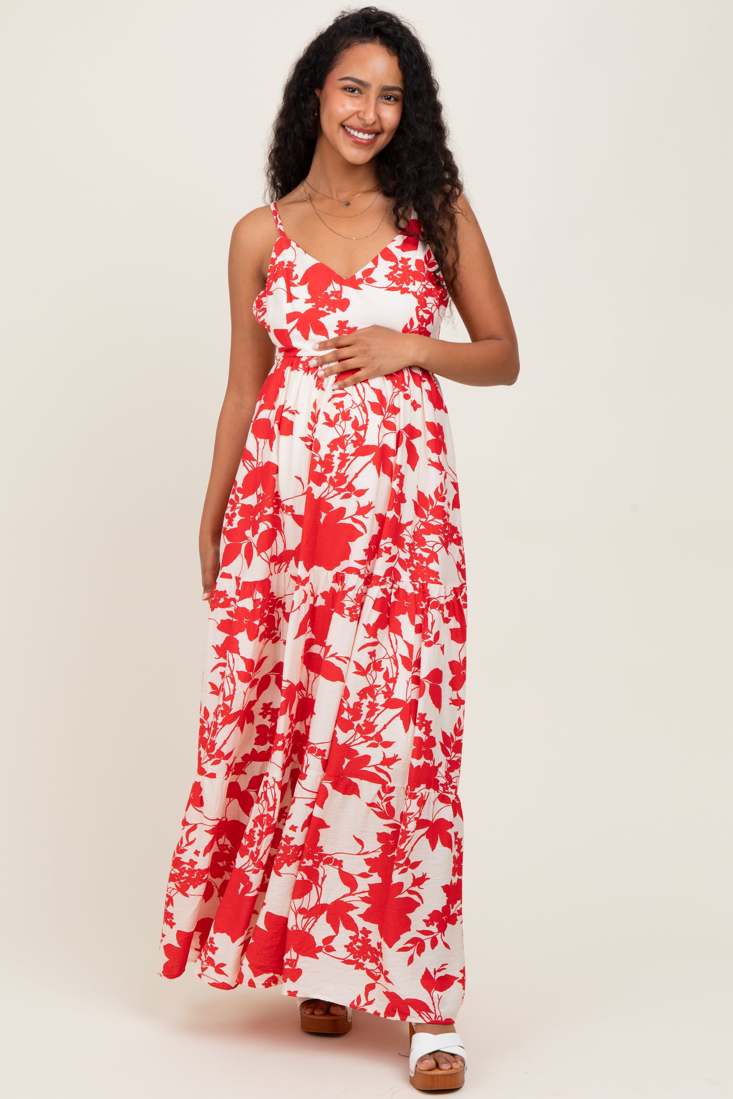 woman wearing a red and white floral maternity maxi dress with spaghetti straps and holding her baby bump