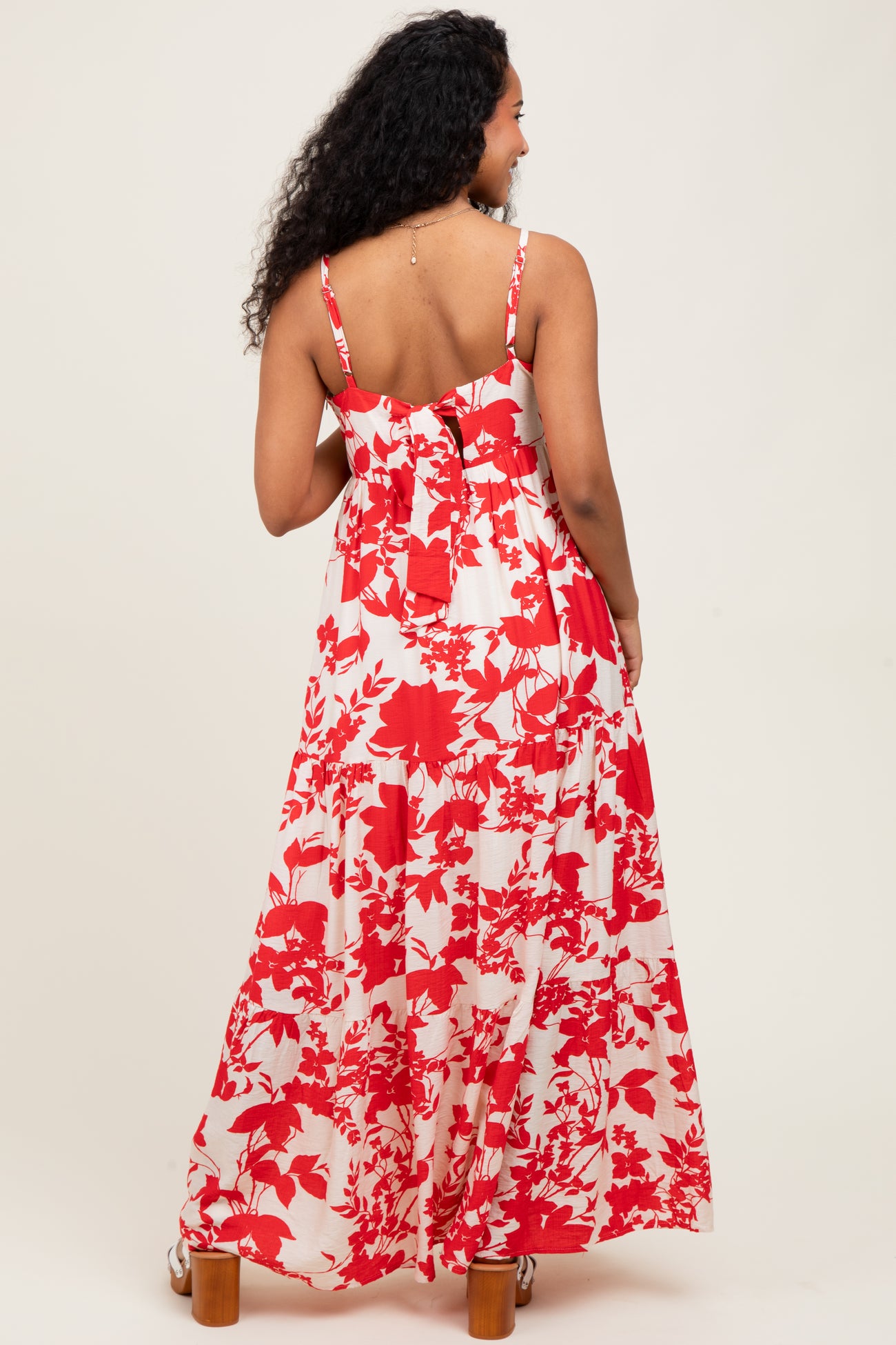 woman wearing a red and white floral maxi maternity dress, with adjustable spaghetti straps and a flowy design