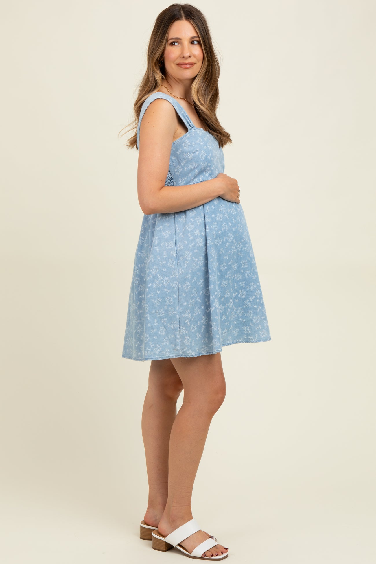 woman wearing a light blue maternity sundress with floral print and holding her baby bump