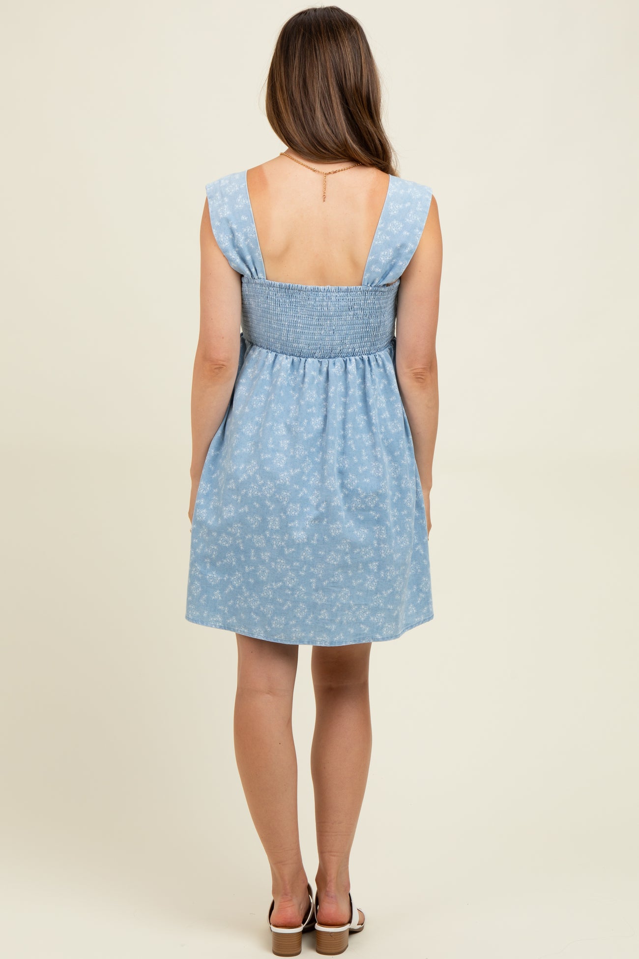 woman wearing a light blue maternity sundress with a smocked back and floral pattern, showing her back
