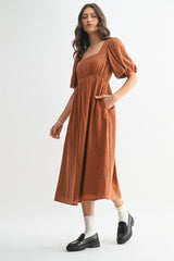 woman wearing a rust-colored midi dress with puff sleeves and side pockets, styled with black loafers and ankle socks
