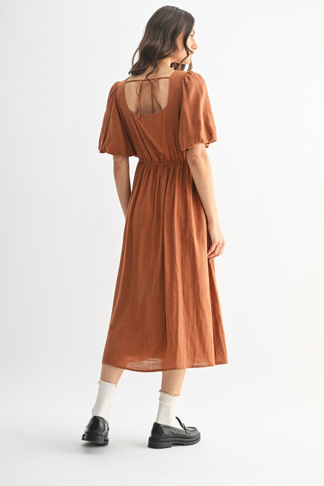 woman wearing a rust colored midi dress with puff sleeves and an open back, standing with her back to the camera