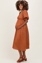 woman wearing a rust colored maternity dress with short puff sleeves and a fitted bodice, gently cradling her baby bump