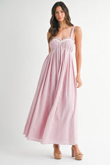 woman wearing a light pink maxi dress with adjustable straps and ruffle details, standing on a plain background