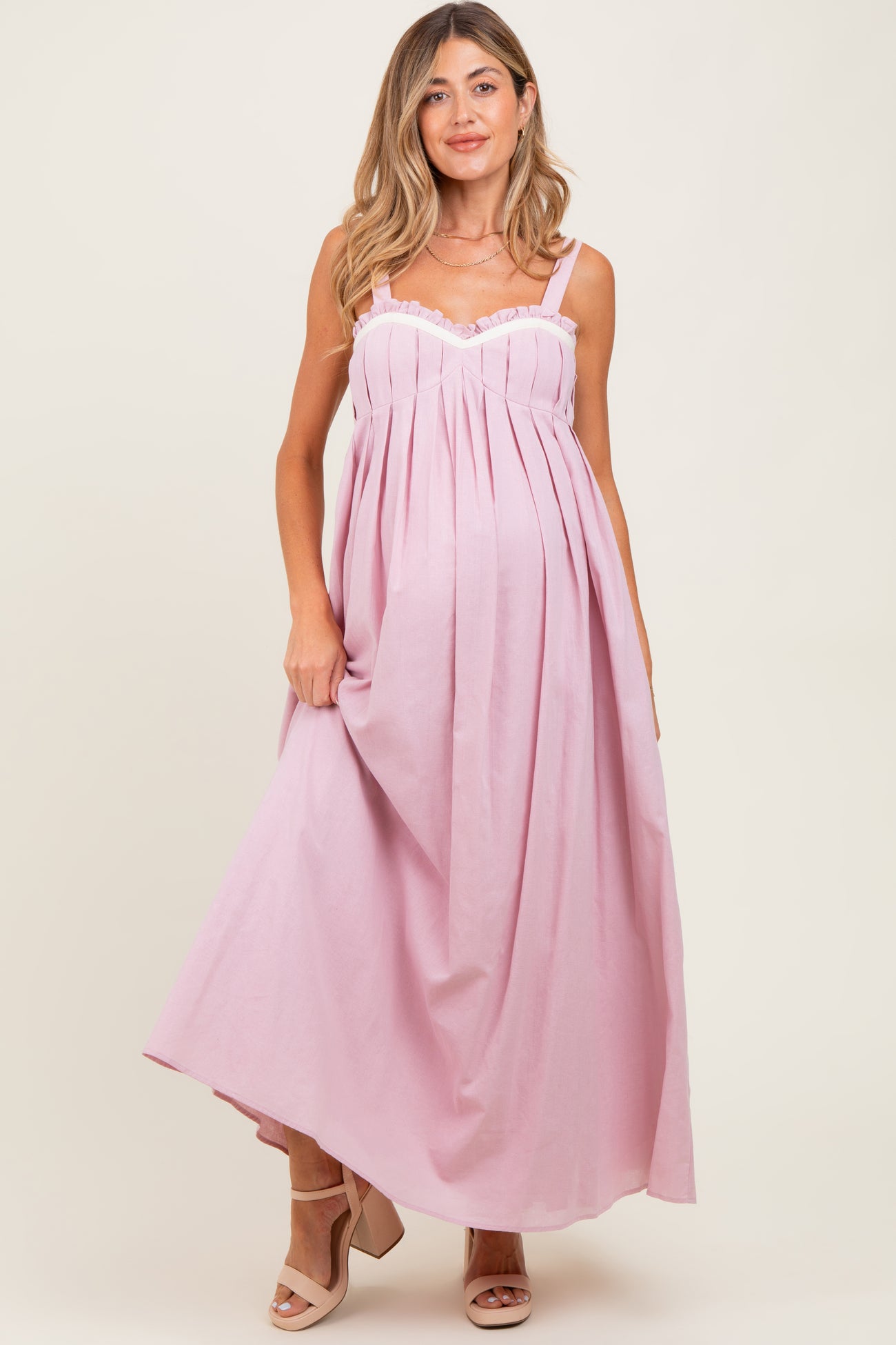 woman wearing a light pink maternity maxi dress with lace detailing and a visible baby bump