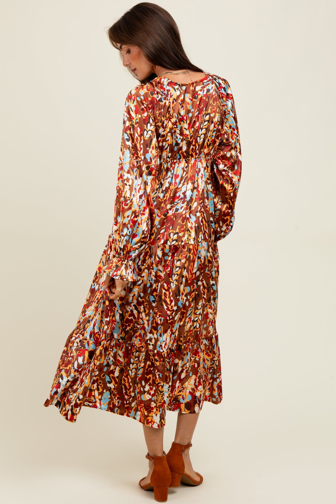 woman wearing a long floral print dress in shades of red, orange, and blue, with a keyhole back and flared sleeves
