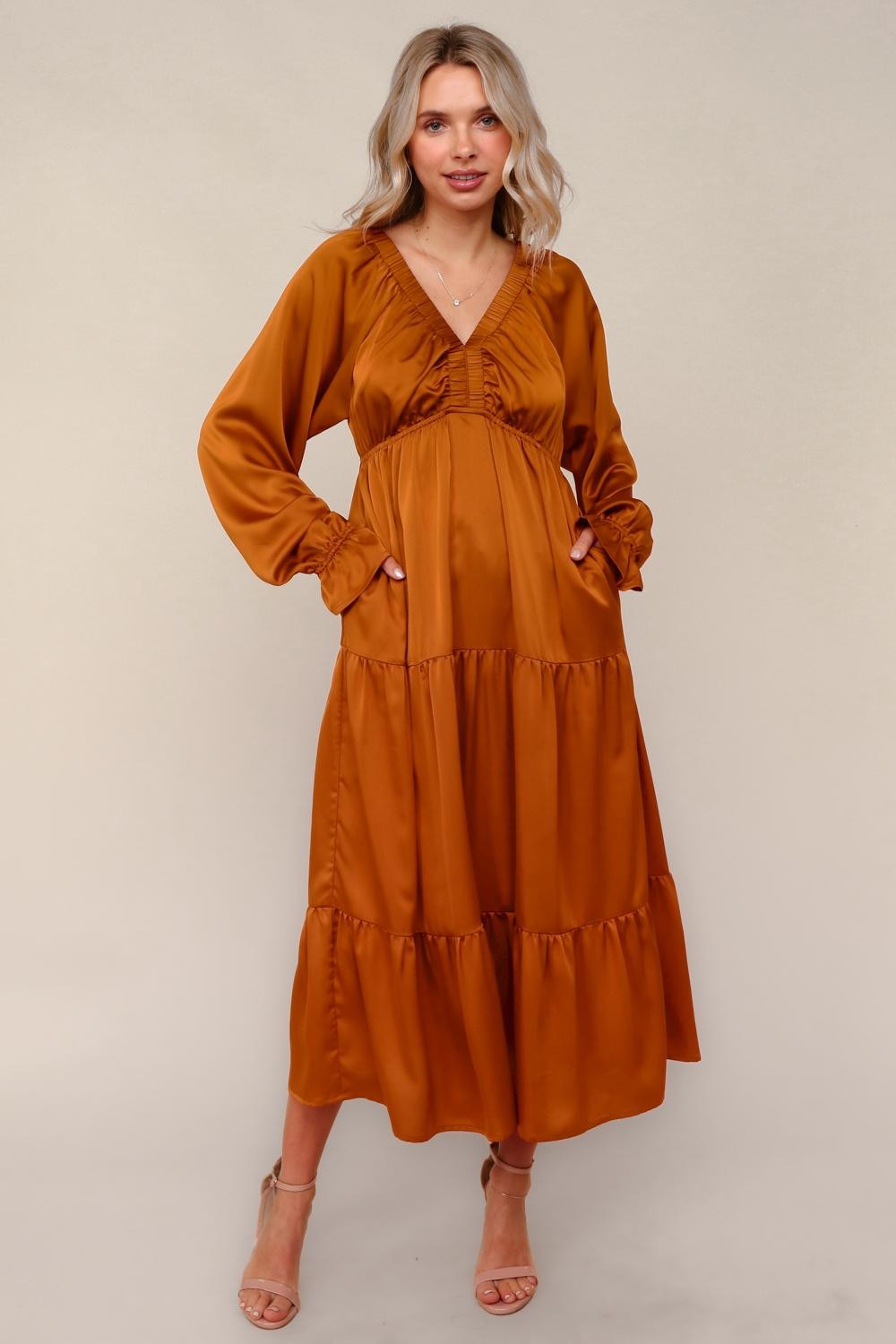 woman wearing an amber long sleeve maxi dress with a tiered design and pockets, standing on a neutral background