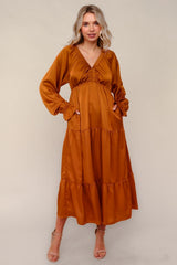 woman wearing an amber long sleeve maxi dress with a tiered design and pockets, standing on a neutral background