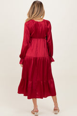 woman wearing a long red satin maternity dress with a tiered skirt and long sleeves, showing a baby bump from the back