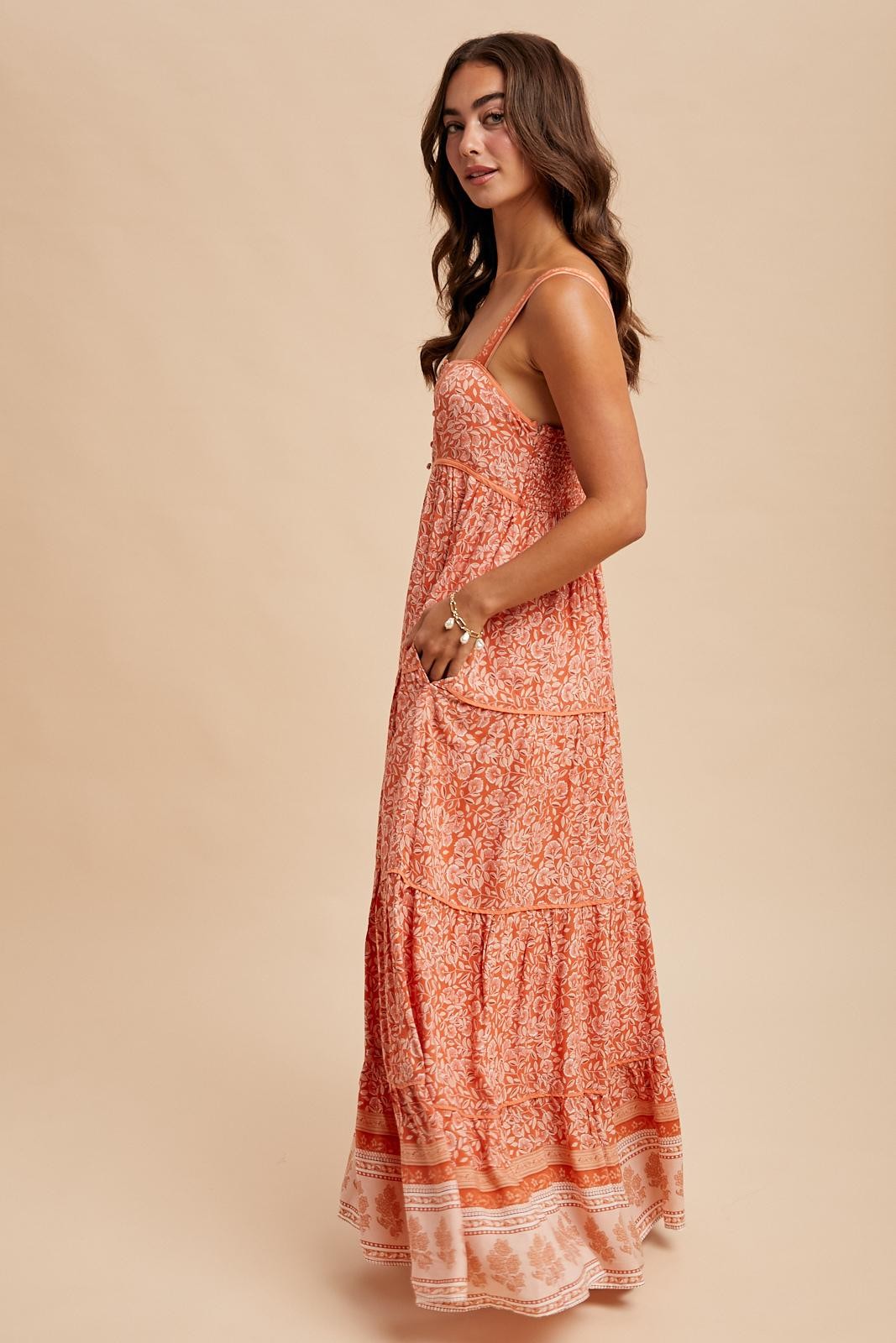 woman wearing an orange patterned maxi dress with a tiered design and spaghetti straps