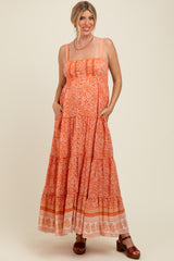 woman wearing an orange patterned maternity maxi dress with tiered details and pockets, smiling while showcasing her baby bump