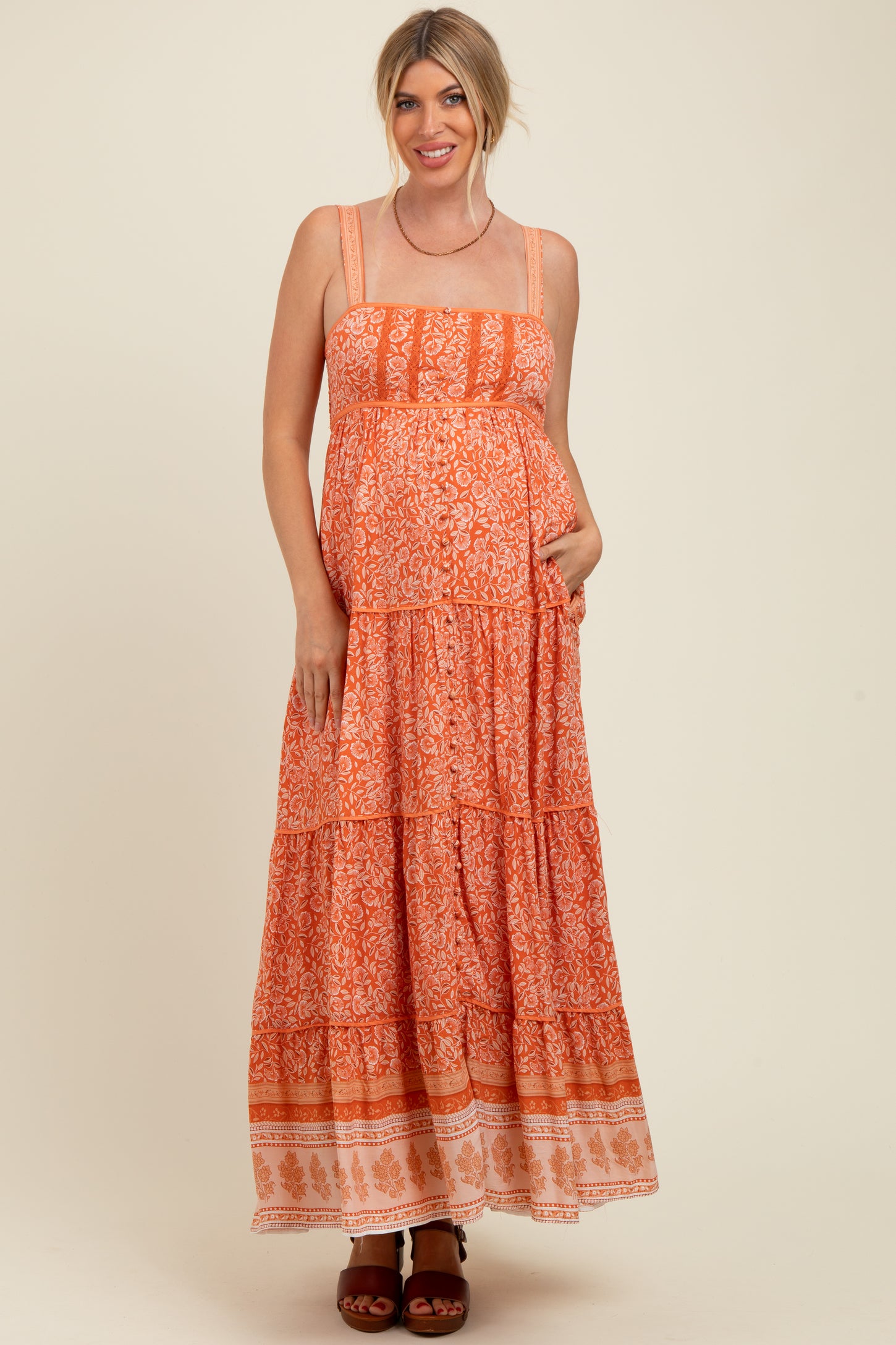 woman wearing an orange floral maxi maternity dress with tiered design and pockets, showcasing her baby bump