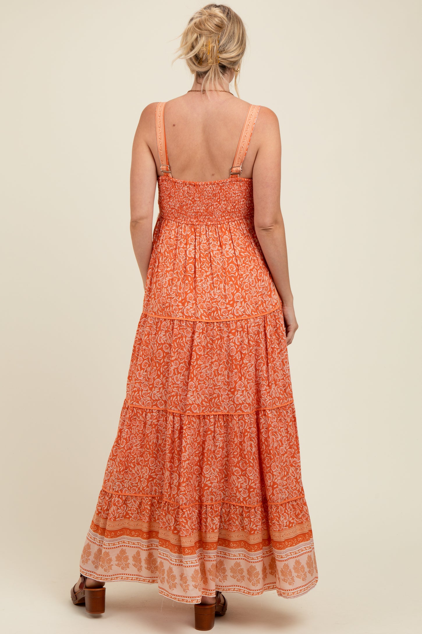 woman wearing an orange patterned maternity maxi dress with smocked bodice and tiered skirt, shown from the back