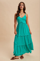 woman wearing a teal tiered maxi dress with thin straps and textured detailing, standing confidently against a neutral background