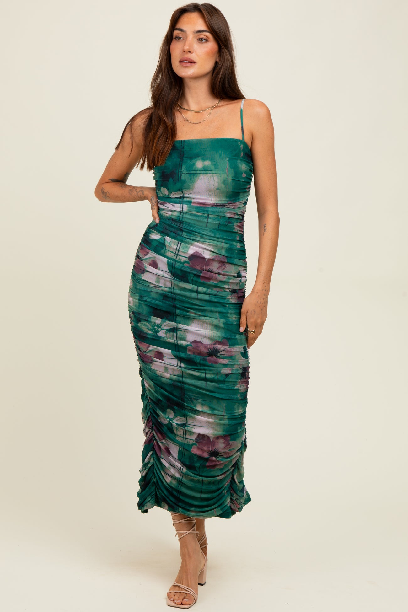 woman wearing a green and purple floral print bodycon midi dress with ruching and spaghetti straps