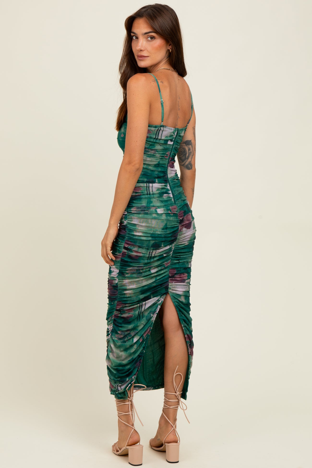 woman wearing a green and purple printed midi dress with ruched details and a thigh-high slit, viewed from the back