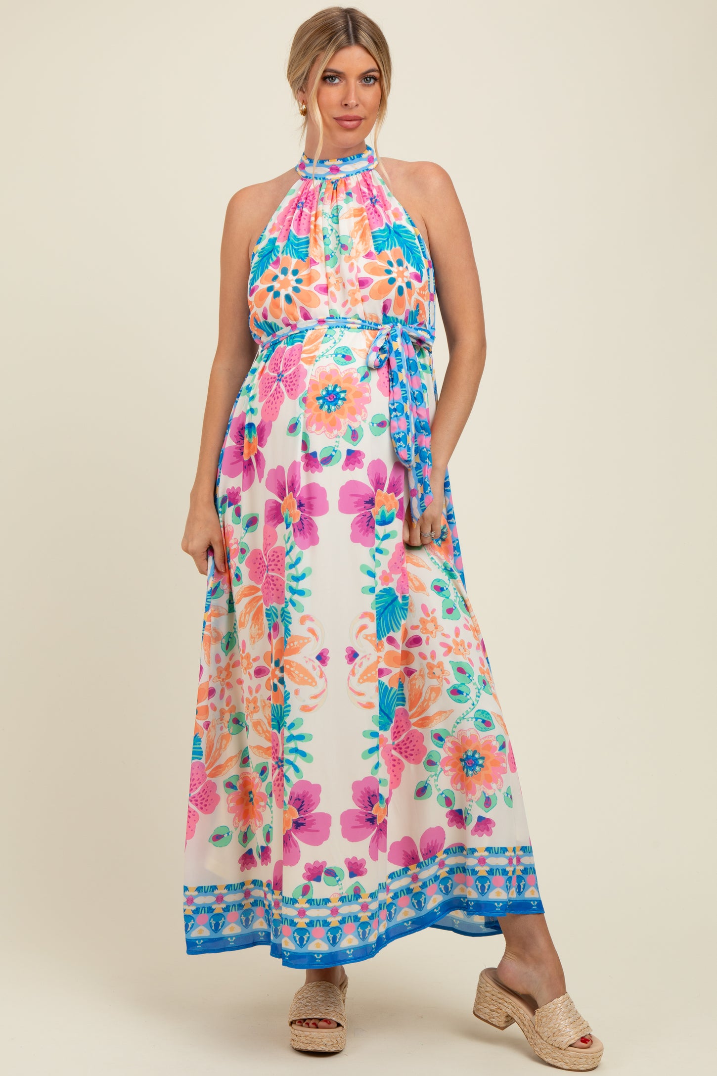 woman wearing a colorful floral halter neck maternity maxi dress with a flowing skirt and a baby bump visible