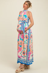 woman wearing a vibrant floral printed maternity maxi dress with halter neck and tie waist, showing her baby bump
