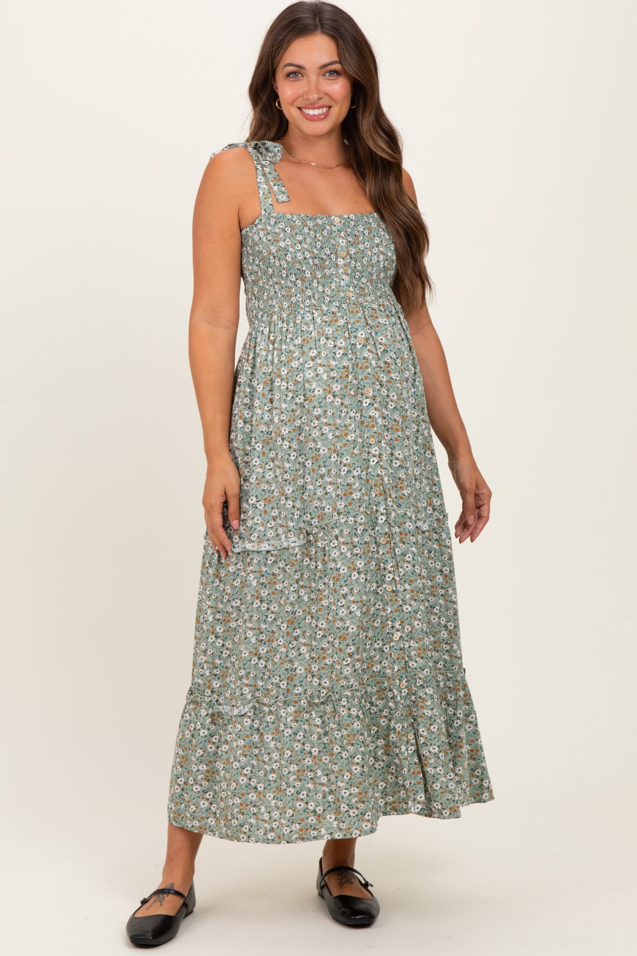 woman wearing a green floral maternity maxi dress with a square neckline and tie shoulder straps, showing her baby bump