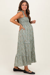 woman wearing a green floral maternity maxi dress with ruffled straps and pockets, showcasing her baby bump