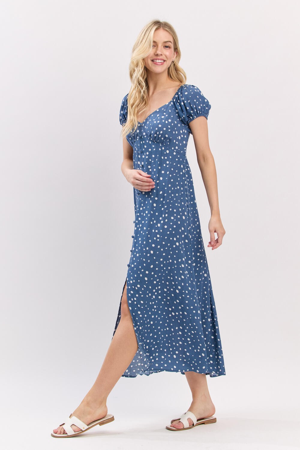 woman wearing a blue polka dot maxi dress with puff sleeves and a side slit, smiling and holding her baby bump
