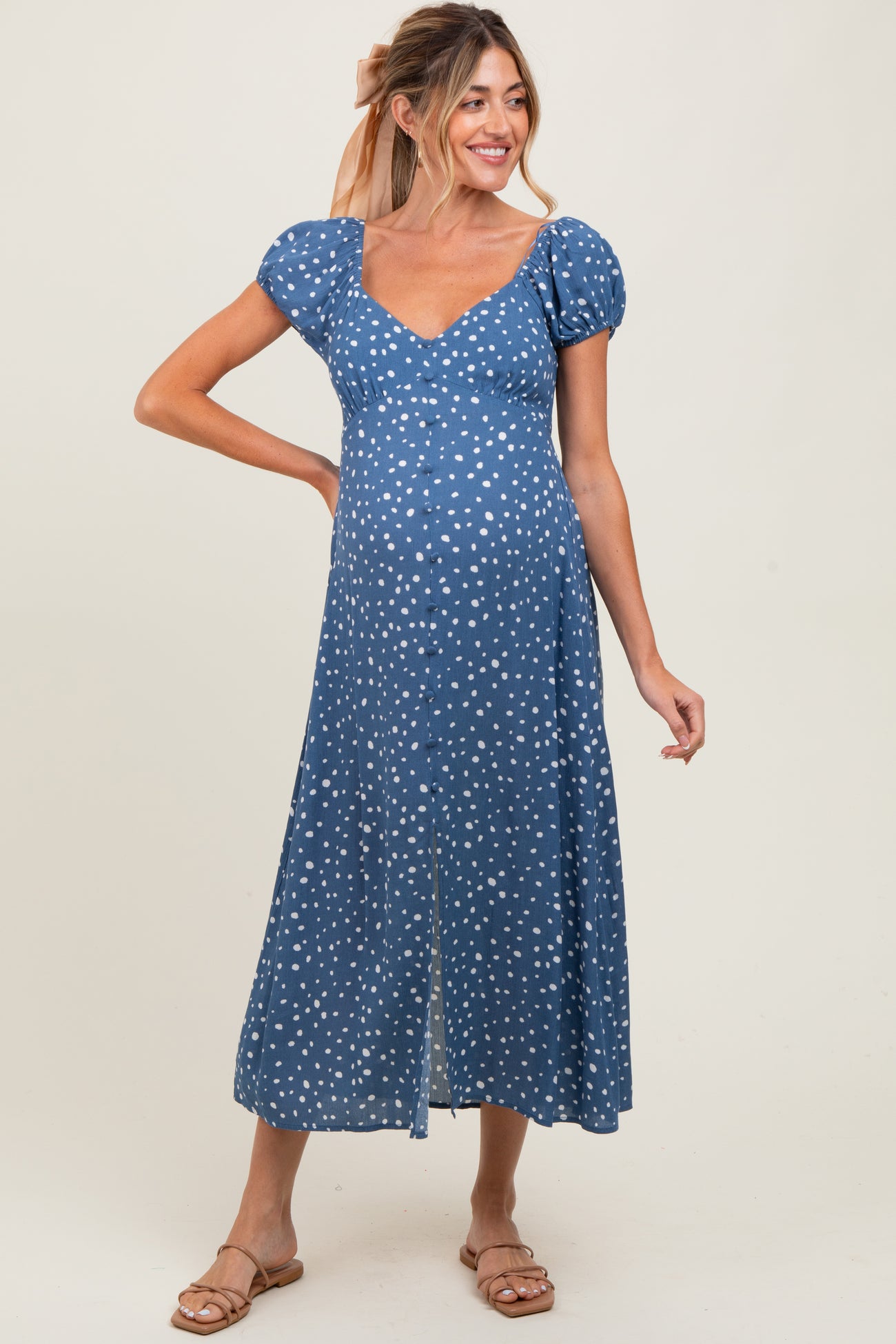 woman wearing a blue polka dot maternity dress with puff sleeves and a front slit, showing her baby bump