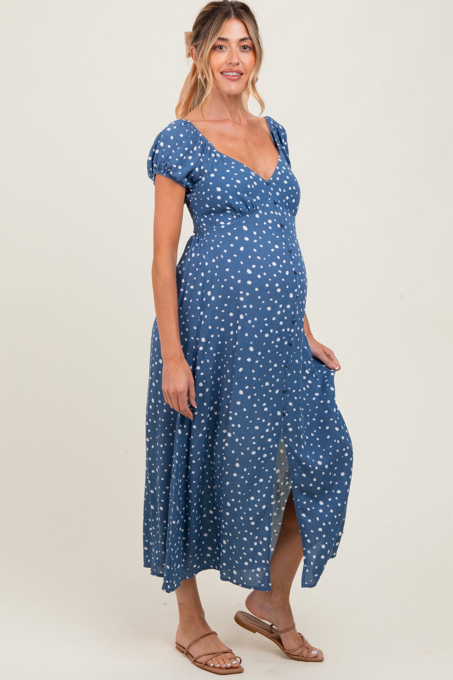 woman wearing a blue polka dot maternity maxi dress with a v-neck and short puff sleeves, showcasing her baby bump