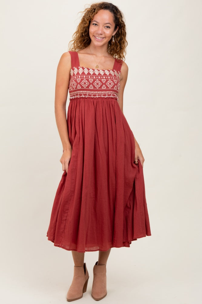 woman wearing a rust-colored maxi dress with embroidered bodice and flowing skirt, smiling and posing