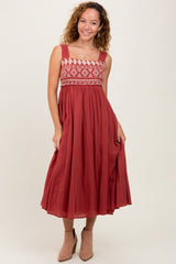 woman wearing a rust-colored maxi dress with embroidered bodice and flowing skirt, smiling and posing