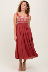 woman wearing a rust-colored maxi dress with embroidered bodice and a flowing skirt, standing against a neutral background
