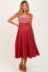 woman wearing a red maternity dress with embroidered bodice and a flowing skirt, showcasing her baby bump