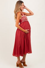 woman wearing a red maternity dress with embroidery, cradling her baby bump and standing in profile