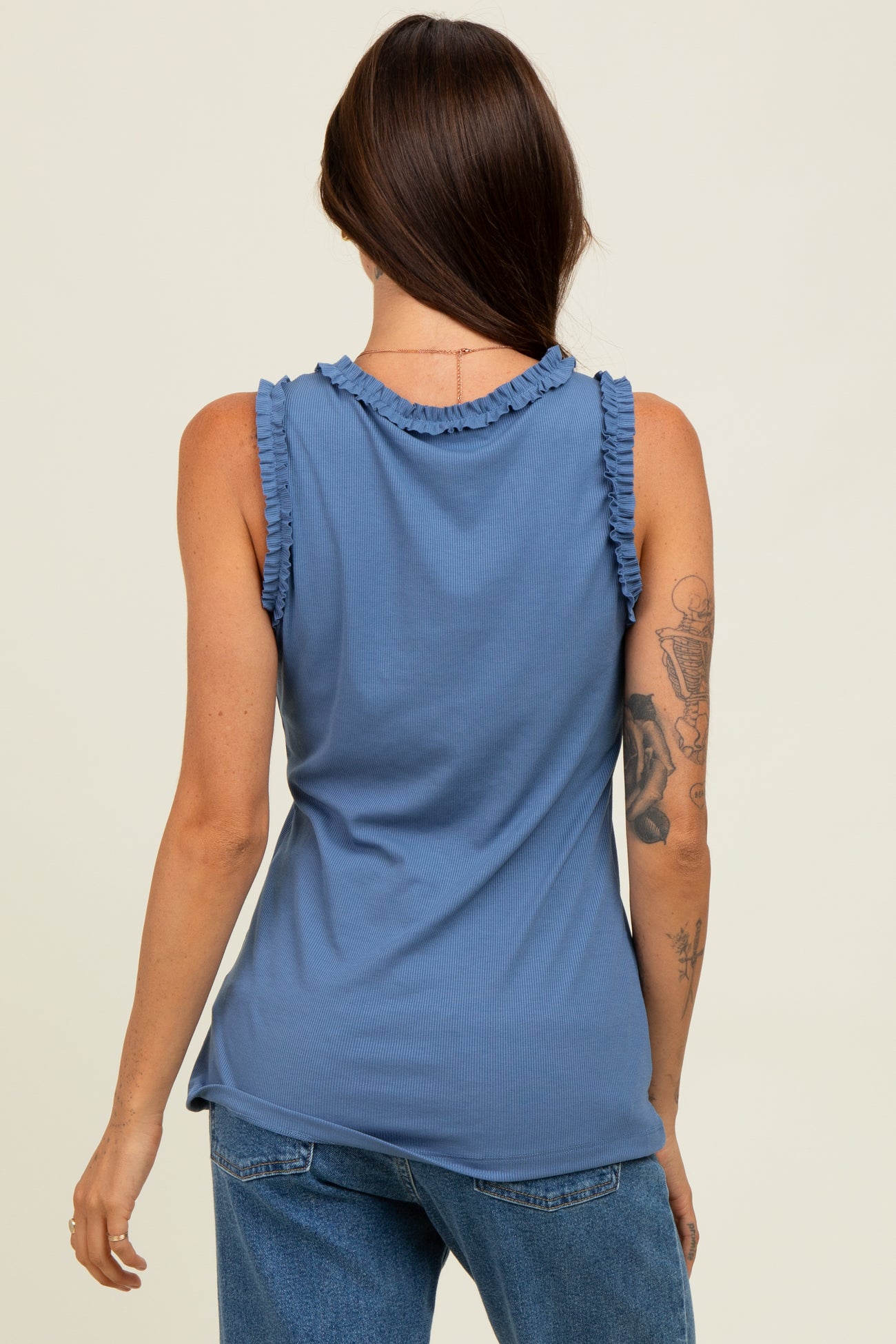 woman wearing a blue sleeveless top with ruffle details on the neckline, shown from the back