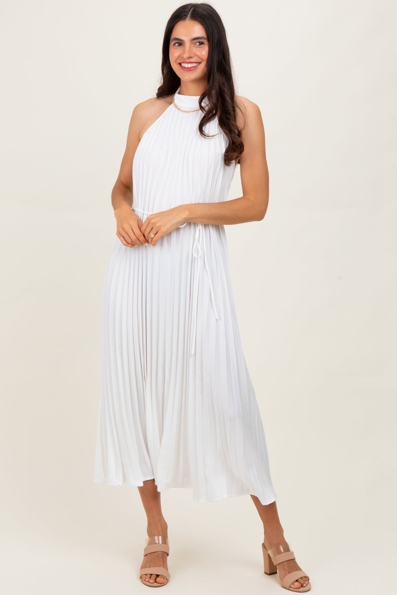 woman wearing a white pleated halter neck dress with a tie waist and heeled sandals