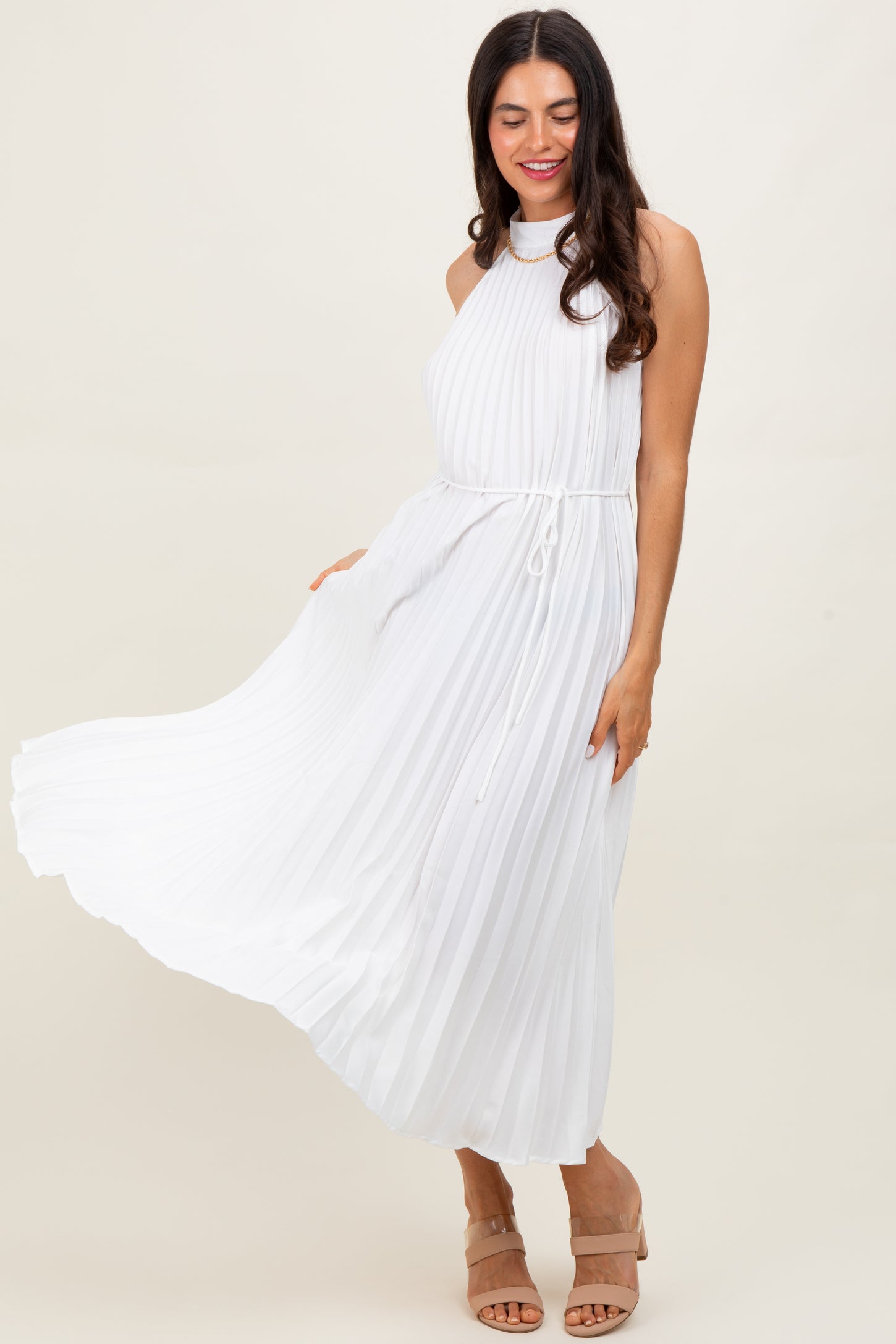 woman wearing a white pleated maxi dress with a halter neckline and tie waist detail