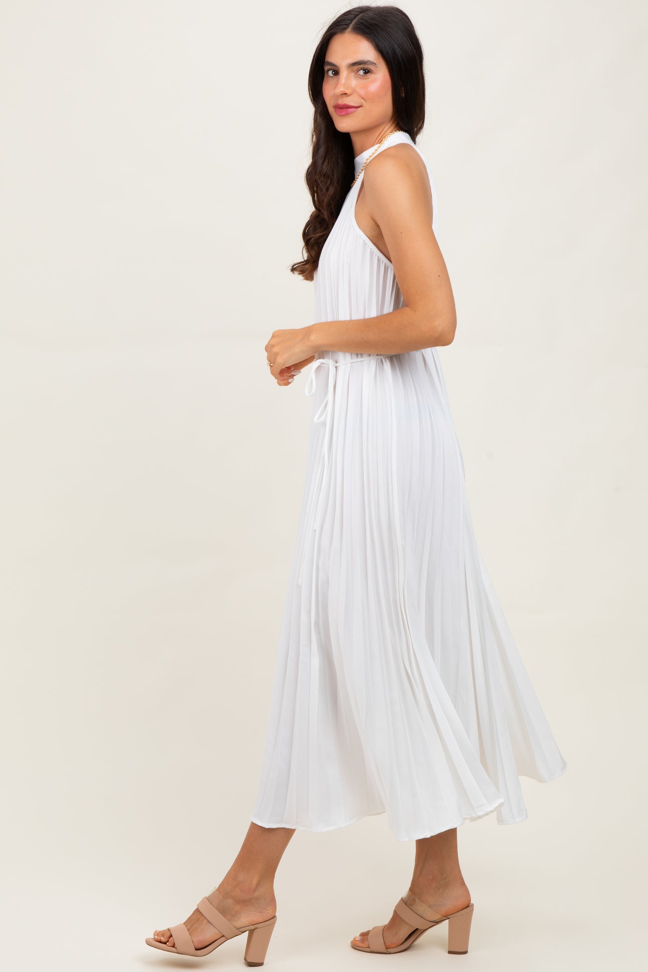 woman wearing a white sleeveless maxi dress with pleated details, styled with beige block-heel sandals