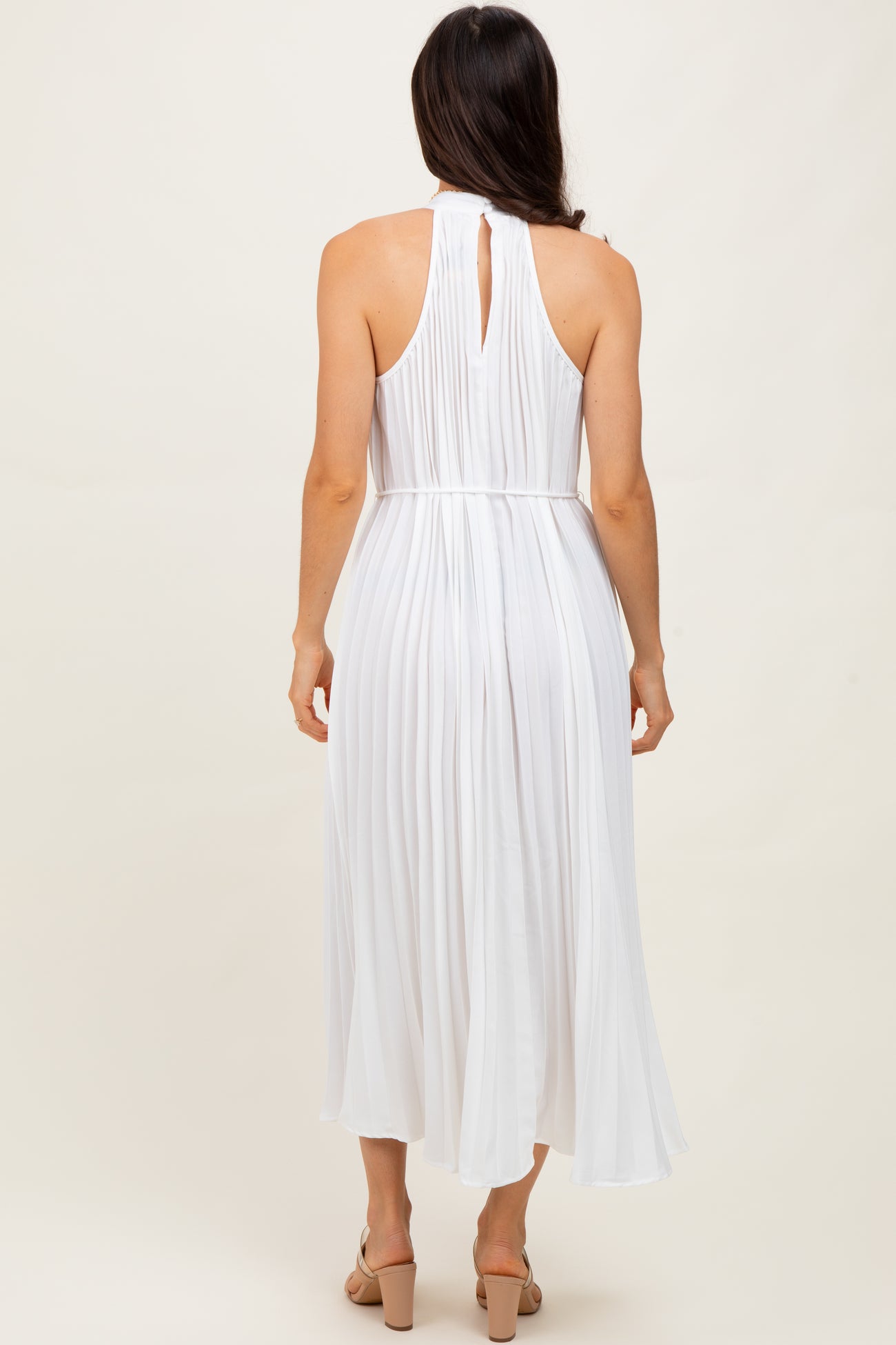 woman wearing a white pleated midi dress with a halter neckline and keyhole back detail
