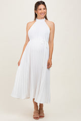 woman wearing a white pleated maternity dress with a halter neck and a tie waist, showing her baby bump