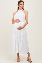 woman wearing a white pleated maternity dress with a tie waist and holding her baby bump