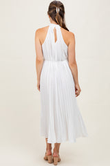 woman wearing a white pleated maternity dress with a halter neck and open back, showing a flowing skirt