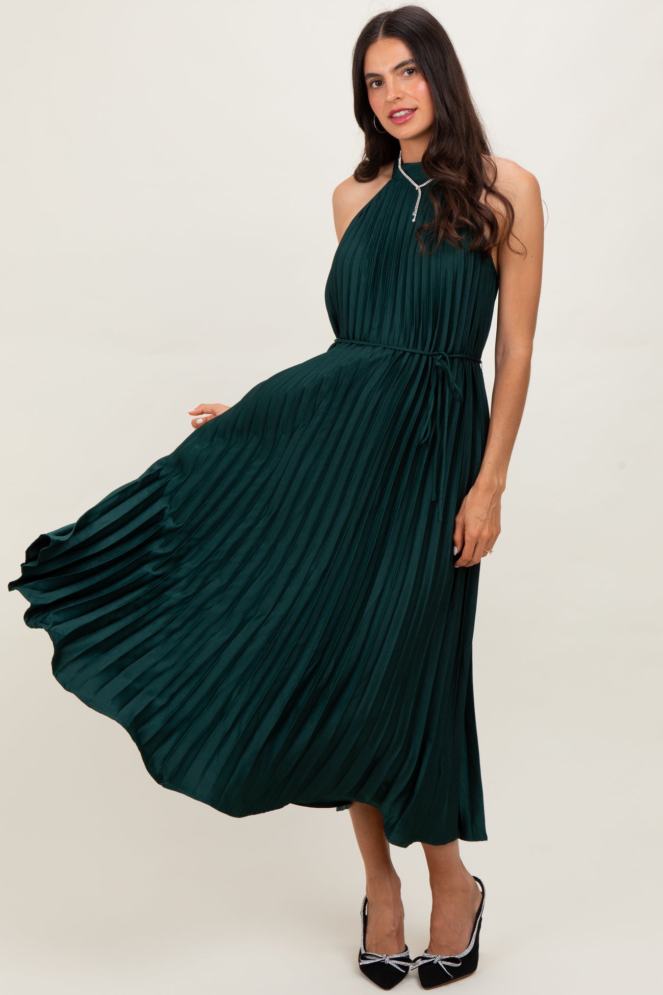 woman wearing a dark green pleated halter neck dress with a tie waist and flowing skirt