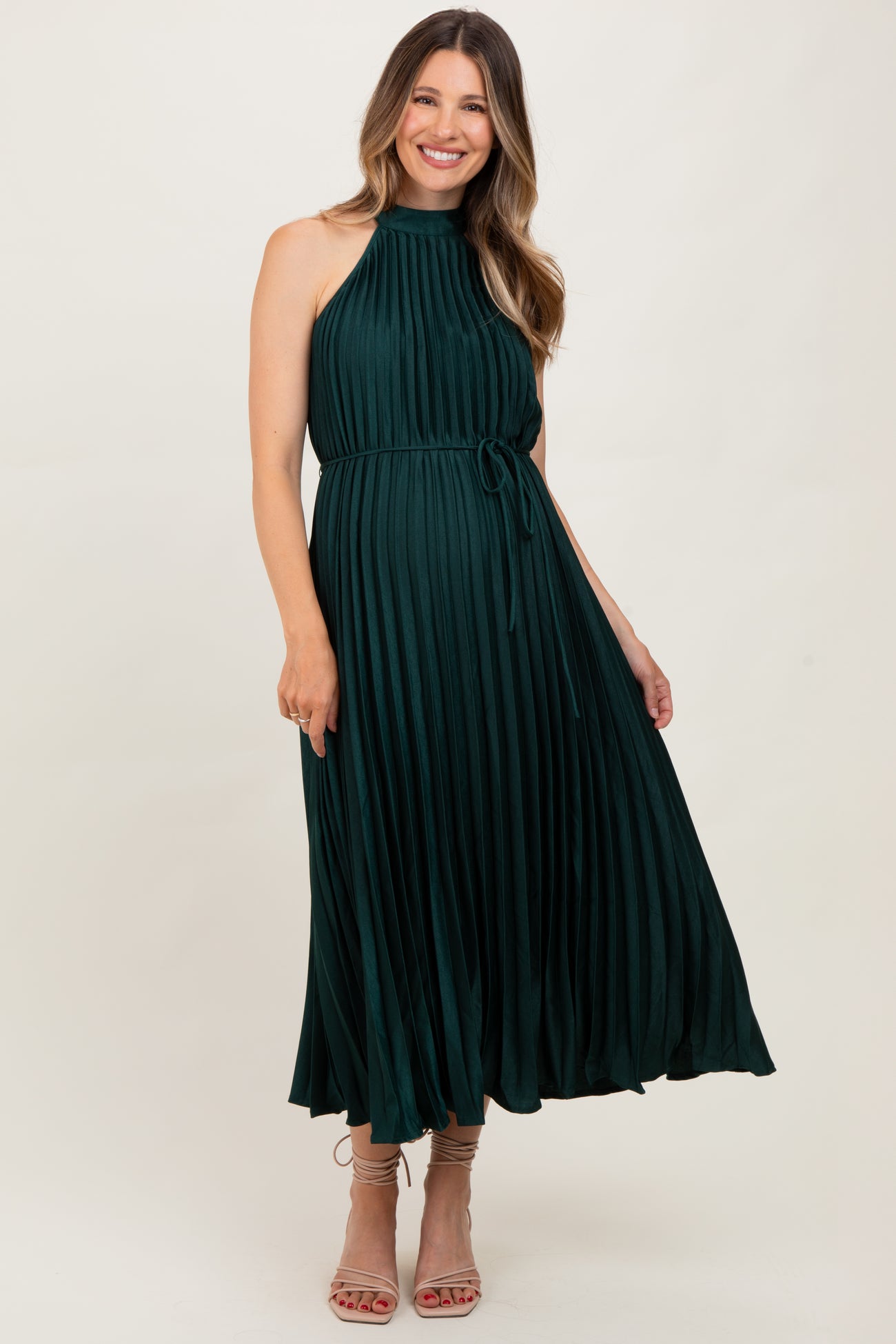 woman wearing a dark green pleated maternity dress with a halter neckline and a tie waist