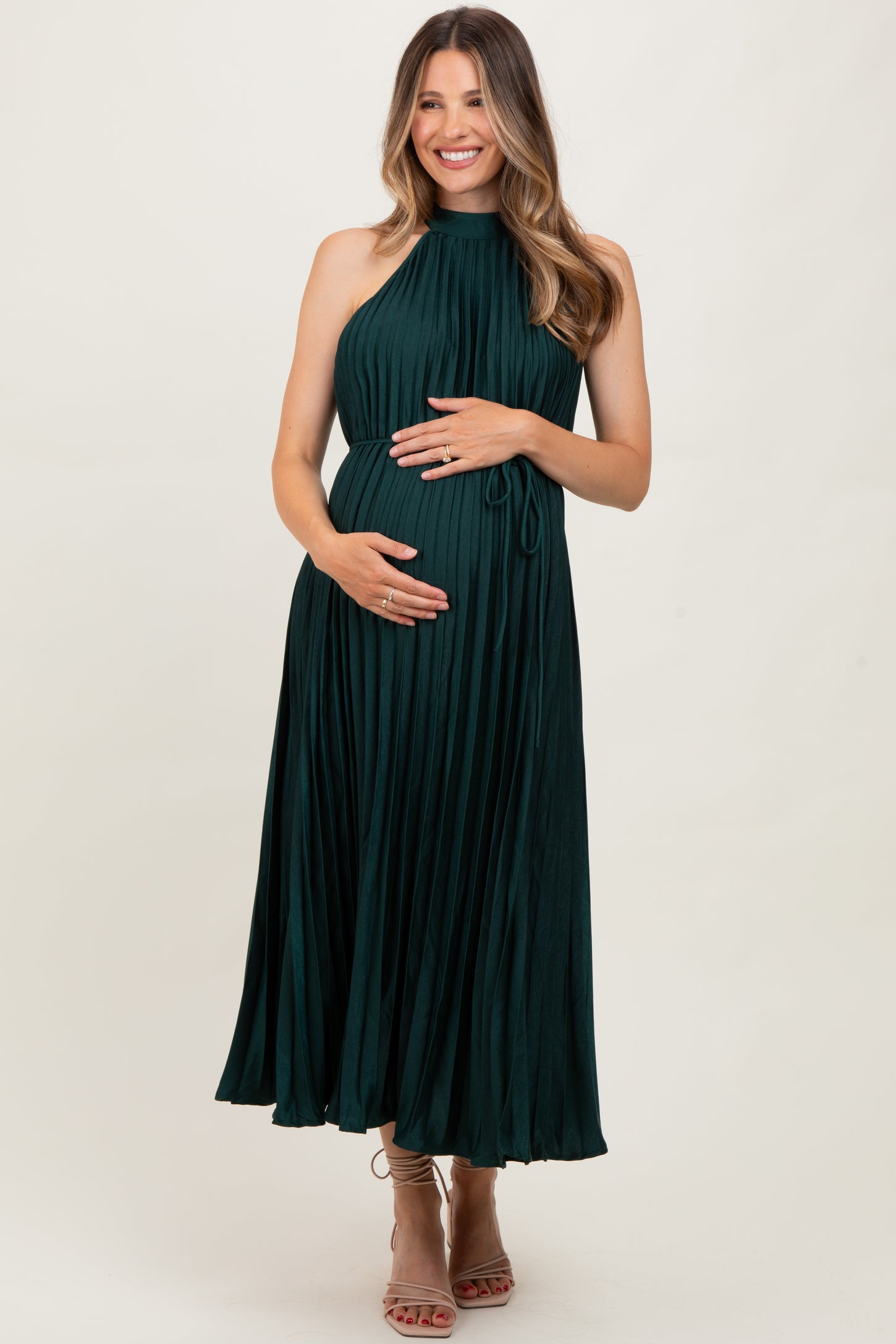 woman wearing a dark green pleated maternity dress and holding her baby bump