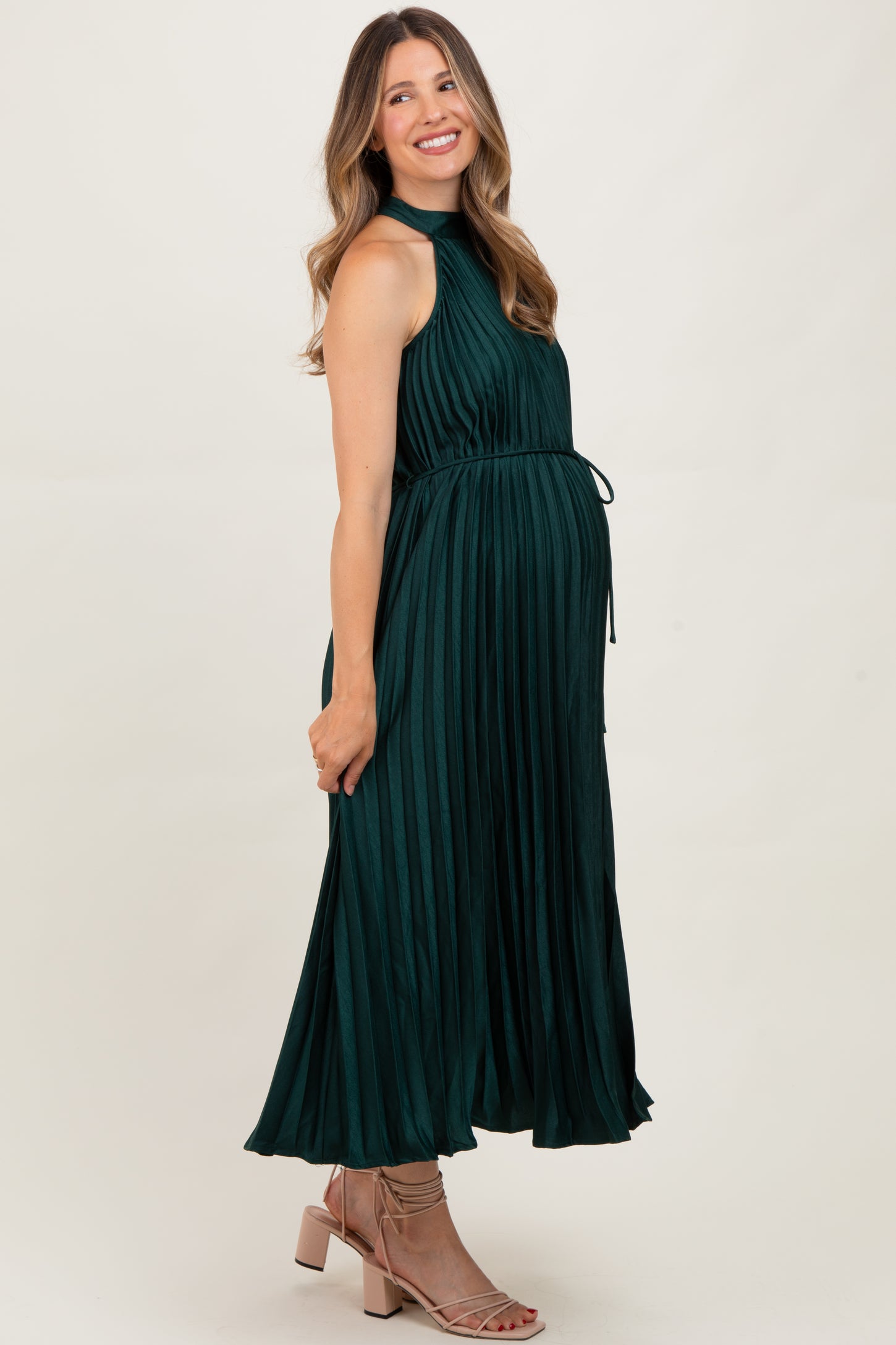 woman wearing a dark green pleated maternity dress with a tie waist and a visible baby bump
