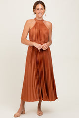 woman wearing an rust-colored pleated halter neck midi dress with a tied waist and smile on her face